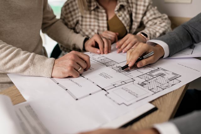 Three people with their hands on a paper showing the blueprint layout of a home